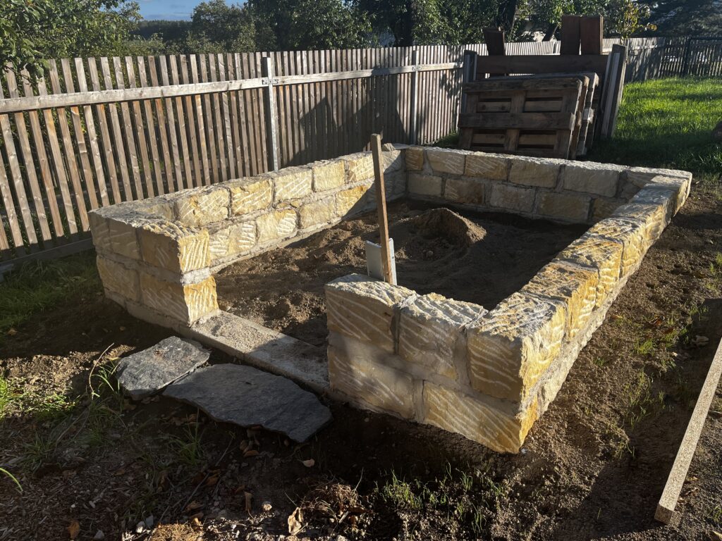 Mauerfundament aus Buntsandstein mit unebener Mauerkrone und Türöffnung für ein geplantes Gewächshaus.