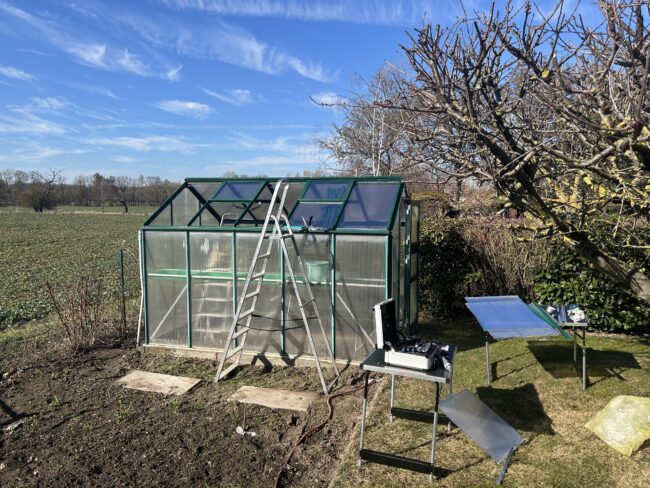 Gewächshaus im Garten während der Dachmontage mit Leiter und Werkzeug