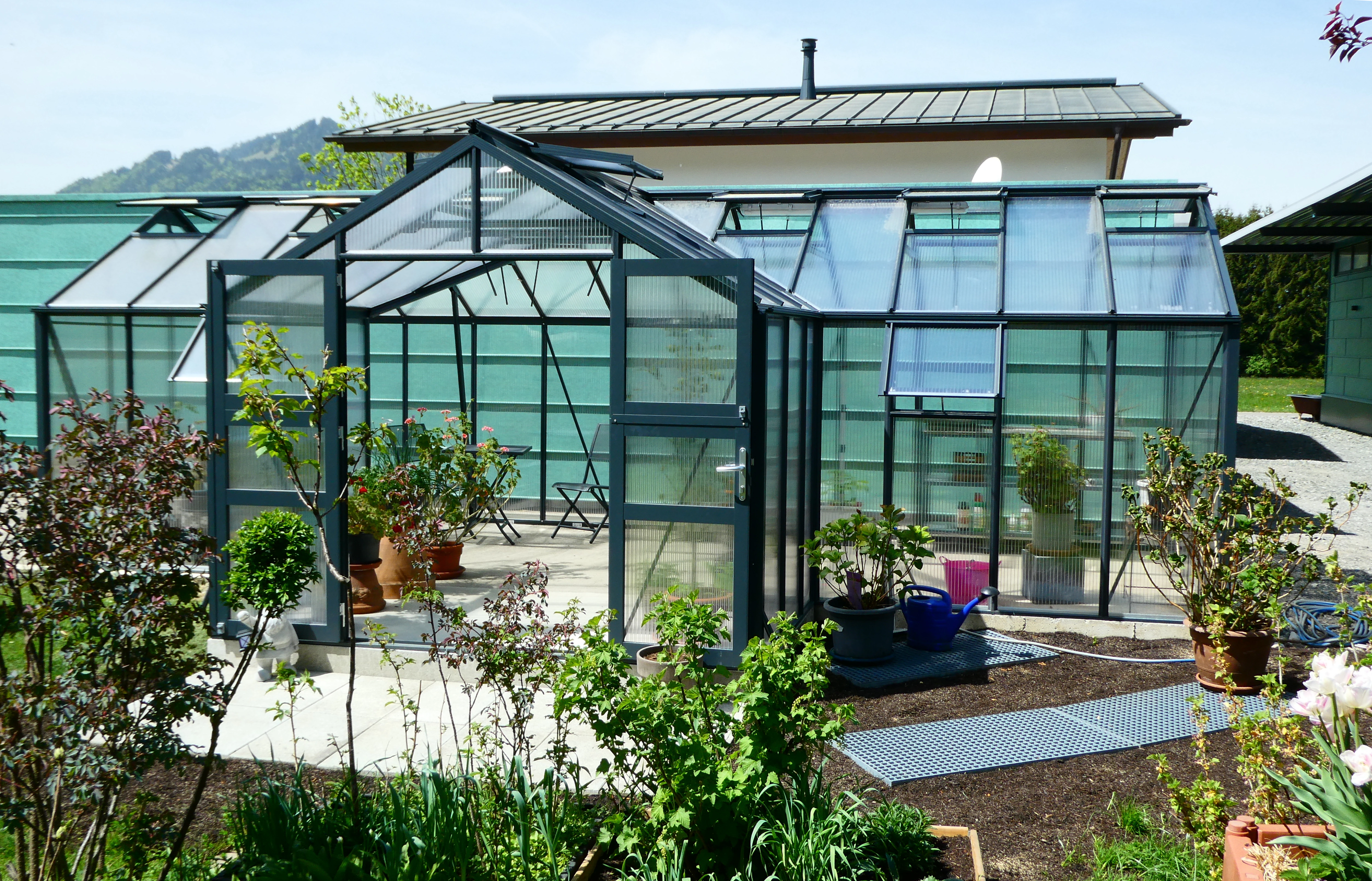 Aluminium Gewächshaus mit Erker, Pflanzkübeln und Zubehör im Gartenbereich.