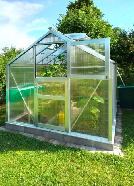 WAMA Gewächshaus MIDI 50 in Alu-Blank mit 10 mm Stegdreifachplatten auf erhöhtem Streifenfundament im Garten.