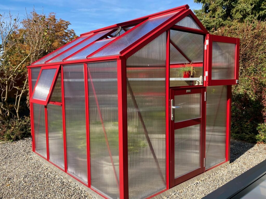 Rotes Gewächshaus mit Aluminium-Fundamentrahmen auf Punktfundament im Privatgarten