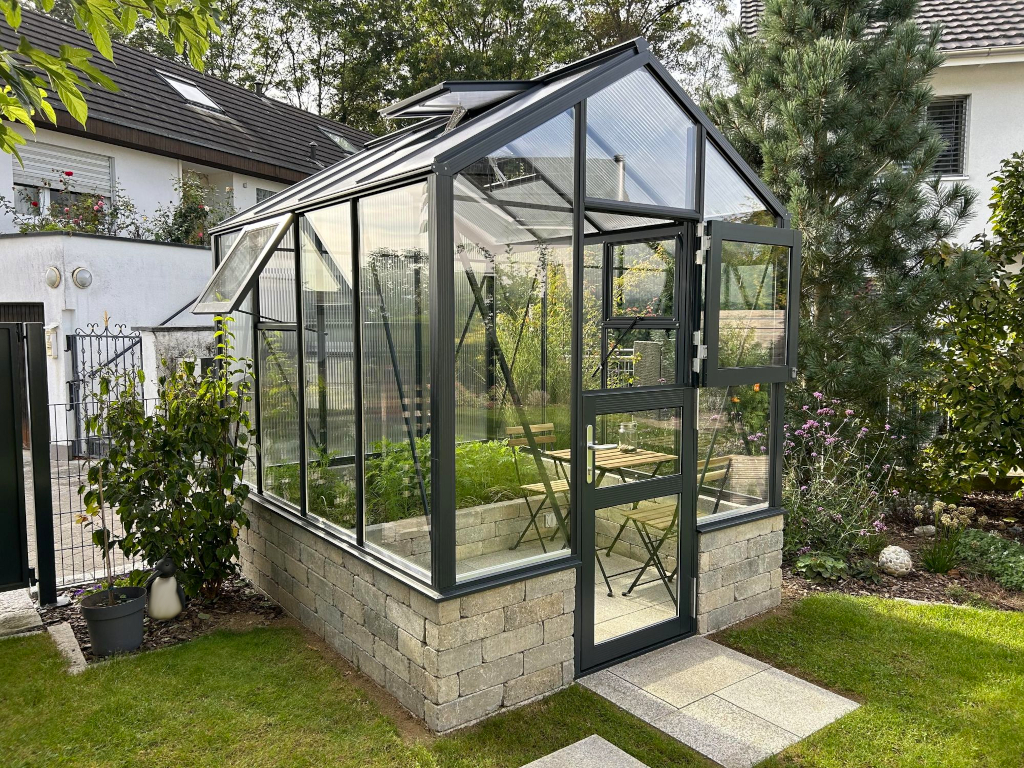 Modernes Gewächshaus aus Glas auf gemauerter Fundamentbasis im Garten